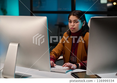 Portrait of successful young woman as female cybersecurity expert using computer in office and looking at screen with blue light 116999334
