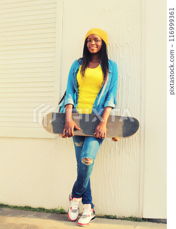 Portrait of happy smiling young african woman with skateboard in the city 116999361