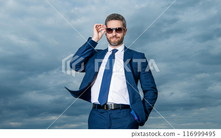 Professional man sky background. Grizzled man adjusting sunglasses. Happy man in suit outdoors Professional man sky background. Grizzled man adjusting sunglasses. Happy man in suit outdoors 116999495