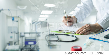 A doctor makes a note while sitting at a desk in a clinic. A doctor makes a note while sitting at a desk in a clinic. 116999610