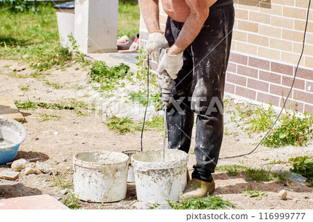House painter stirs fixing adhesive mortar for fake brick external panel. 116999777
