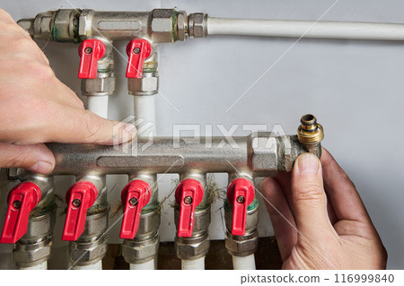 Plumber installing manifold for plastic pipes with five outlets. 116999840