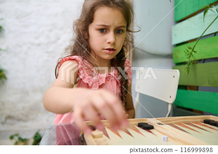 Young girl focused on playing a board game in an outdoor setting 116999898