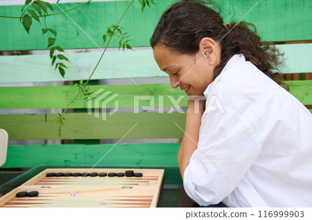 Woman enjoying a game of backgammon in a relaxed outdoor setting Woman enjoying a game of backgammon in a relaxed outdoor setting 116999903