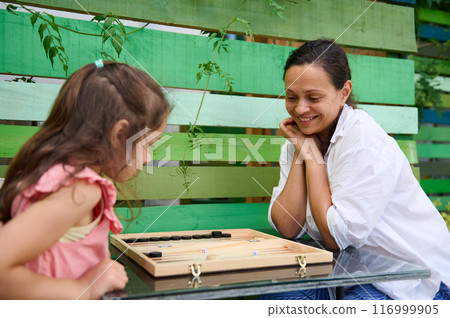 Mother and daughter enjoying a playful backgammon game outdoors 116999905