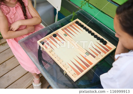 Two children playing a game of backgammon outdoors on a sunny day Two children playing a game of backgammon outdoors on a sunny day 116999913