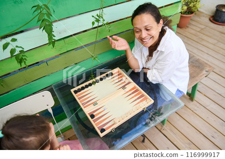 Mother and daughter playing backgammon outdoors on a sunny day, sharing joy and quality time Mother and daughter playing backgammon outdoors on a sunny day, sharing joy and quality time 116999917