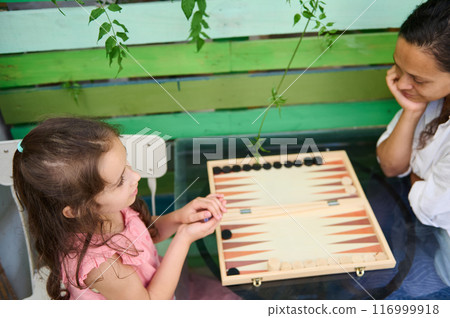 Mother and daughter bond over backgammon game at home. Family and leisure time together Mother and daughter bond over backgammon game at home. Family and leisure time together 116999918