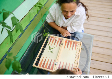Woman playing backgammon on a sunny day outdoors, enjoying leisure time with a friend Woman playing backgammon on a sunny day outdoors, enjoying leisure time with a friend 116999921