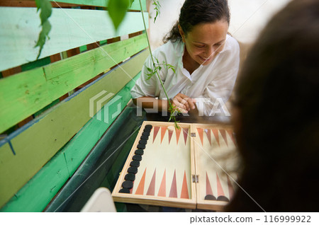 Woman enjoying a game of backgammon outdoors with a friend Woman enjoying a game of backgammon outdoors with a friend 116999922