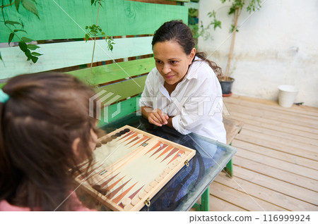 Mother and daughter playing backgammon together outdoors in a cozy family setting 116999924