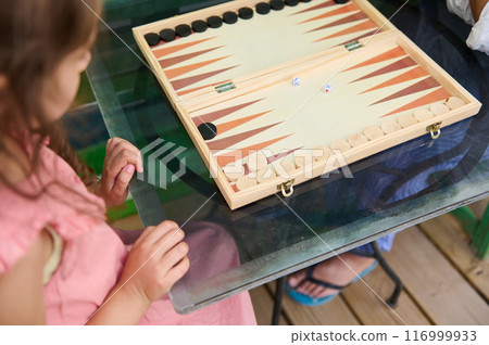 Girl playing backgammon with wooden board and dice indoors 116999933