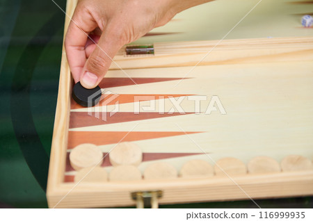 Hand placing chip in backgammon game on wooden board Hand placing chip in backgammon game on wooden board 116999935