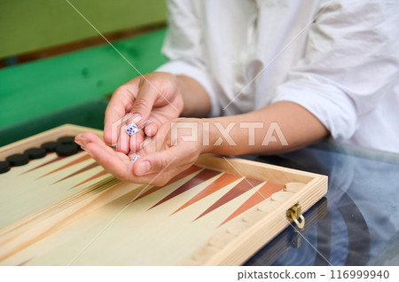 Hands holding dice while playing backgammon on a wooden board Hands holding dice while playing backgammon on a wooden board 116999940