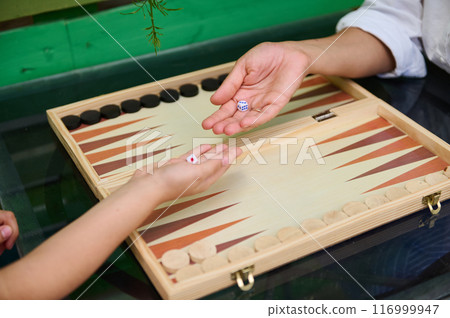 Close-up of two hands playing backgammon with dice on a wooden board game 116999947