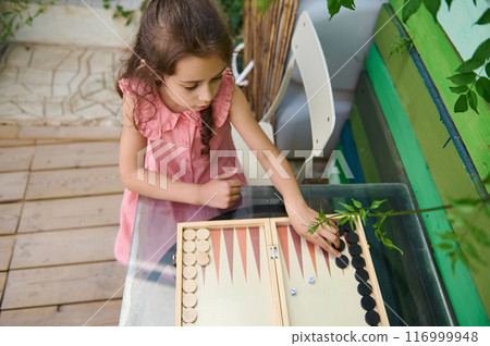 Little girl playing backgammon game outdoors on a sunny day 116999948