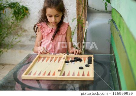 Young girl playing backgammon outdoors on a glass table Young girl playing backgammon outdoors on a glass table 116999959
