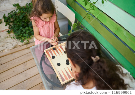 Mother and daughter playing backgammon outdoors at wooden table 116999961