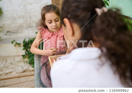 Girl in pink dress engaged in outdoor educational activity guided by another child Girl in pink dress engaged in outdoor educational activity guided by another child 116999962