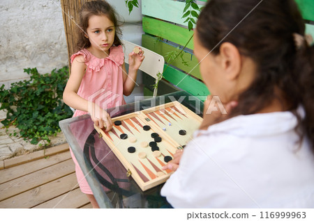 Mother and daughter playing backgammon together in a cozy outdoor setting Mother and daughter playing backgammon together in a cozy outdoor setting 116999963
