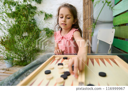 Young girl playing backgammon in a garden setting on a sunny day 116999967
