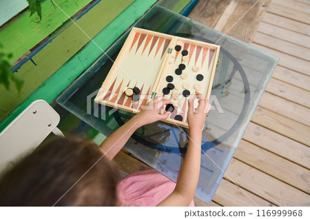 Child playing backgammon at a glass table outdoors on a colorful porch 116999968