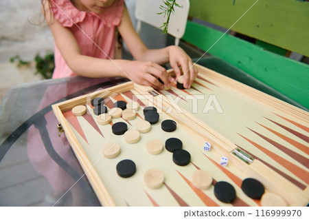 Child playing backgammon on a wooden board in a casual outdoor setting Child playing backgammon on a wooden board in a casual outdoor setting 116999970