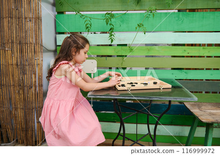 Young girl in pink dress playing a board game outdoors Young girl in pink dress playing a board game outdoors 116999972