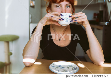 portrait young woman drinking tea or coffee in morning in kitchen 116999973