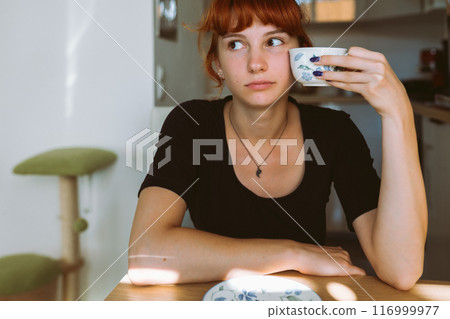 portrait young woman drinking tea or coffee in morning in kitchen portrait young woman drinking tea or coffee in morning in kitchen 116999977