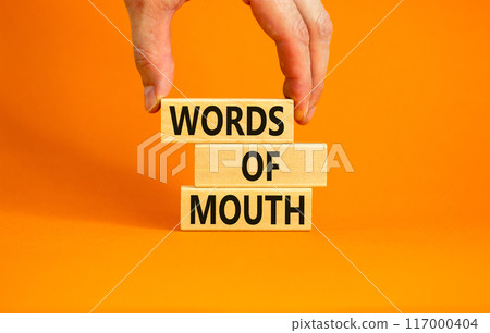 Words of mouth symbol. Concept words Words of mouth on wooden blocks on a beautiful orange table orange background. Businessman hand. Business, finacial and words of mouth concept. Copy space. 117000404