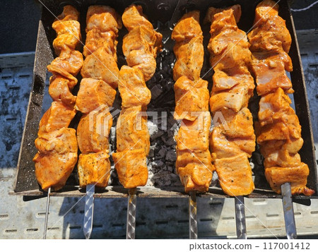 Fresh delicious hot shashlik fried on the grill. Pork meat is cooked on hot coals in a barbecue, rotated on skewers for baking. Fresh delicious hot shashlik fried on the grill. Pork meat is cooked on hot coals in a barbecue, rotated on skewers for baking. 117001412