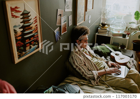 High angle shot of tired male student chilling on comfortable single bed while checking his social networks 117003170
