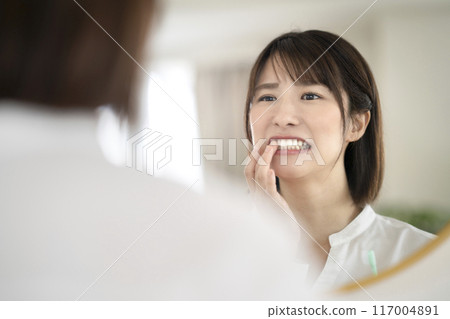 A woman in her 30s checking her gums while brushing her teeth A woman in her 30s checking her gums while brushing her teeth 117004891