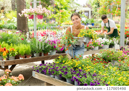 Girl admiring blooming potted calibrachoa in garden store 117005498