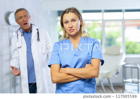 Upset middle-aged nurse standing with her back to angry doctor Upset middle-aged nurse standing with her back to angry doctor 117005599