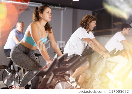 Man and woman taking indoor cycling class at fitness center, doing cardio riding bike 117005622