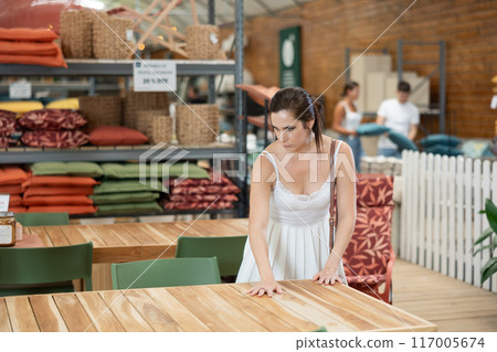 Thoughtful brunette choosing wooden patio table at garden center 117005674