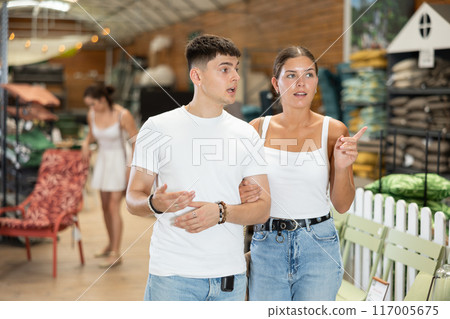 Married couple look for something in room garden furniture store, searching for item to complete patio. Woman with husband buyers looks around in showroom Married couple look for something in room garden furniture store, searching for item to complete patio. Woman with husband buyers looks around in showroom 117005675