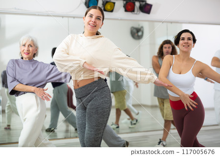 Smiling young woman rehearsing modern dance with group in dance school Smiling young woman rehearsing modern dance with group in dance school 117005676
