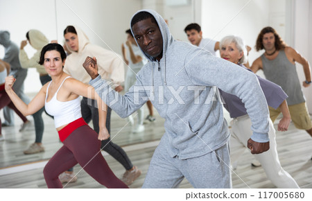 African-american guy practising dance moves with other people in dance studio 117005680