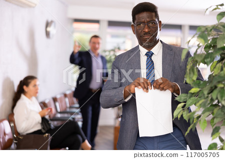 Upset middle-aged man standing in waiting room with his back to person who is shouting at him 117005705