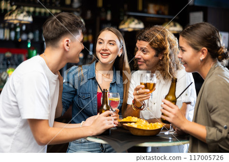 Happy friends drinking beer and chatting with each other in restaurant Happy friends drinking beer and chatting with each other in restaurant 117005726