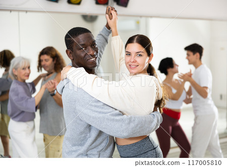 African man and caucasian lady rehearsing latin paired dance moves 117005810