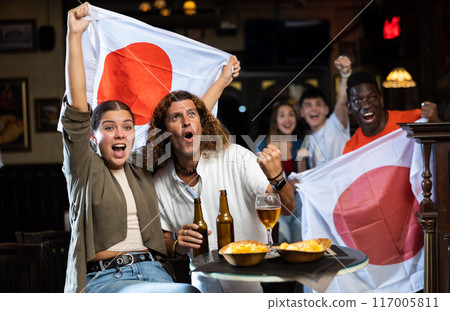 Group of happy fans celebrate victory of their favorite team with flag of Japan in beer bar 117005811