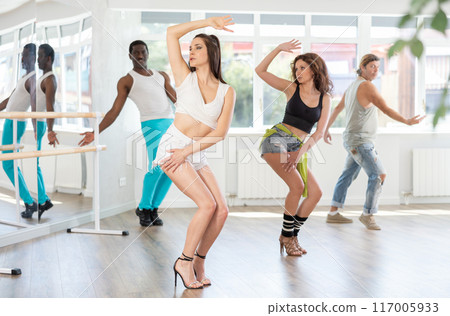 Female dancers at dance lesson in stiletto heels, in different choreographic poses, showing off their slim body in dance studio Female dancers at dance lesson in stiletto heels, in different choreographic poses, showing off their slim body in dance studio 117005933
