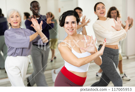 Cheerful young lady learning new modern dance in group dance lesson 117005953