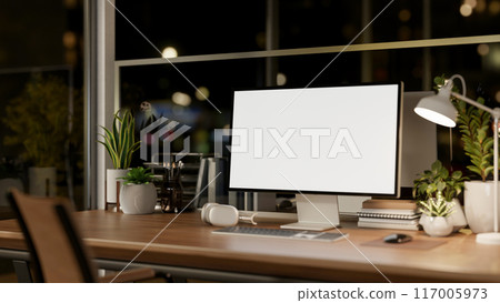 A computer mockup on a wooden table in a modern office at night, illuminated by a table lamp. A computer mockup on a wooden table in a modern office at night, illuminated by a table lamp. 117005973