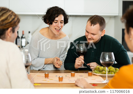 Friends drinking wine and enthusiastically playing board game at home 117006016