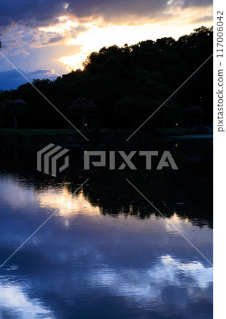 Summer 2024: Evening view of Sagiike Ukimido in Nara Park - The sun setting over the mountainside in gold and the water reflecting the blue sky ⑤ 117006042